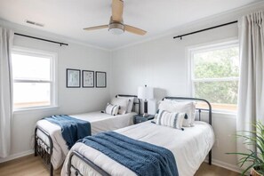 Ein Schlafzimmer mit zwei Einzelbetten, einem Deckenventilator, einem Fenster mit Vorhängen und gerahmten Bildern an der Wand.