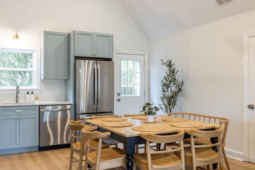 A modern kitchen with light blue cabinets, stainless steel appliances, and a wooden dining table with chairs.