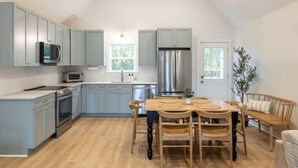 A kitchen with light blue cabinets, a wooden dining table, and a ceiling fan. - Newly Renovated, 1 min walk to beach, 3rd Row Emerald Isle Beach House (Emerald Isle)