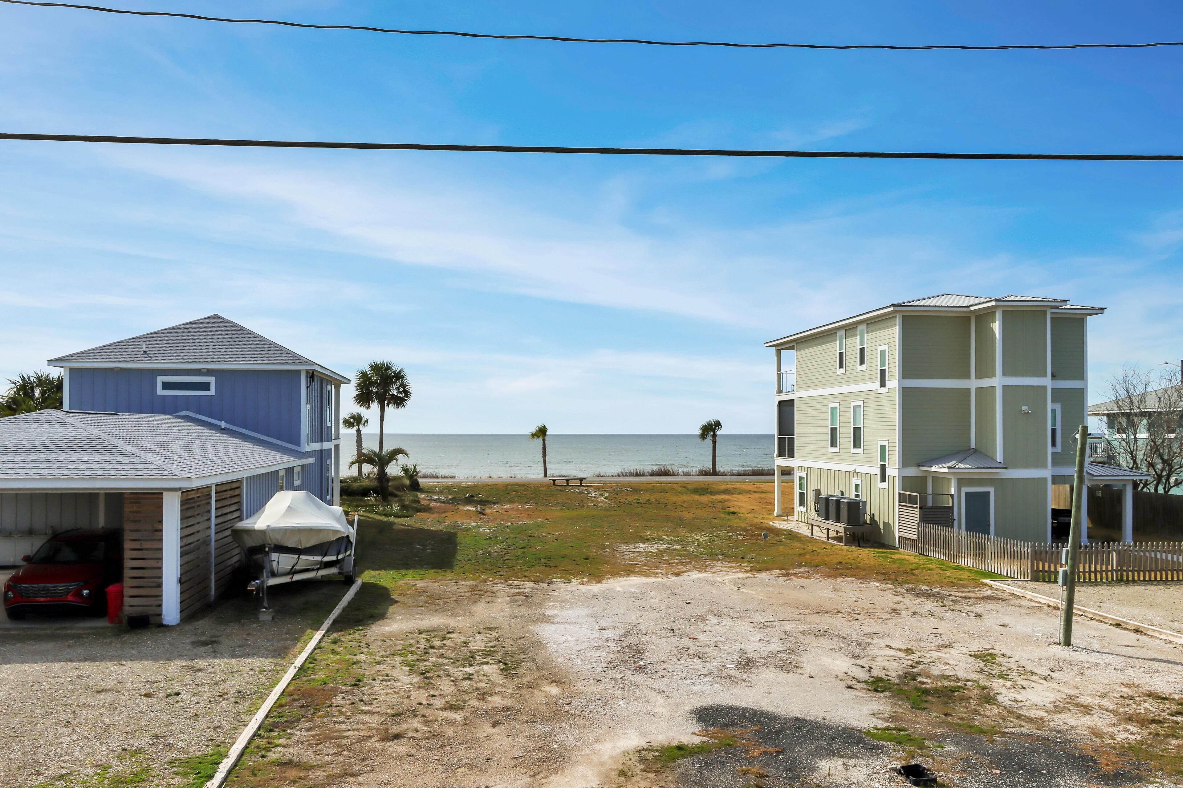 A coastal residential area with two-story houses, a sandy driveway, and a view of the ocean.