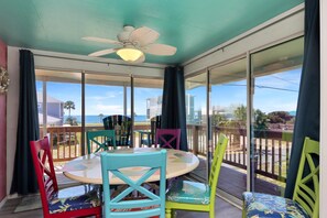 A sunlit room with a round table and colorful chairs, large windows with a view of the beach, and a ceiling fan. - Sea Shell (Port St. Joe)