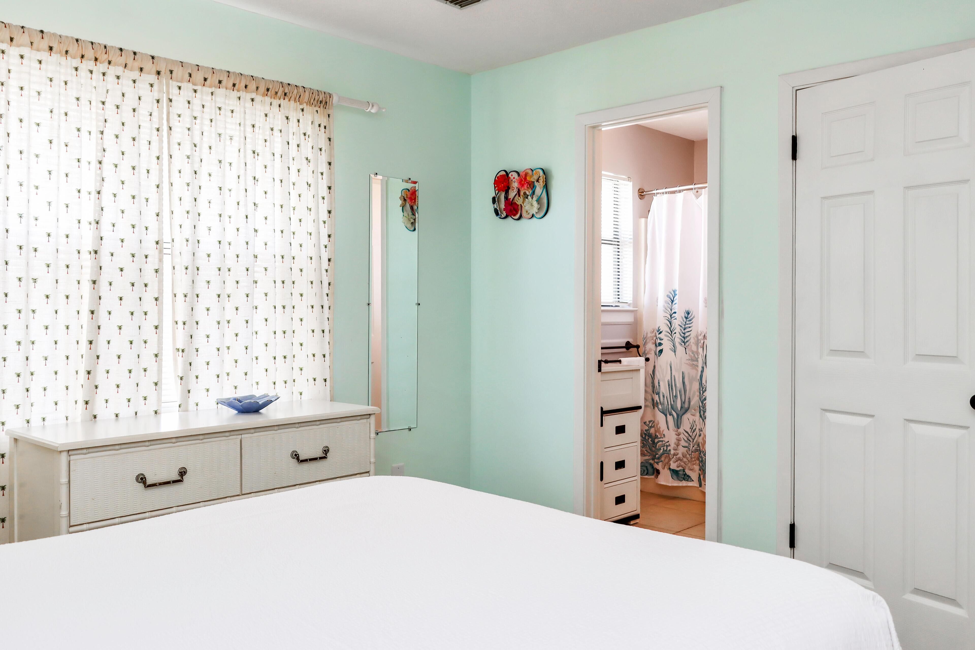 A bedroom with a bed, a dresser, a mirror, and a door leading to another room.