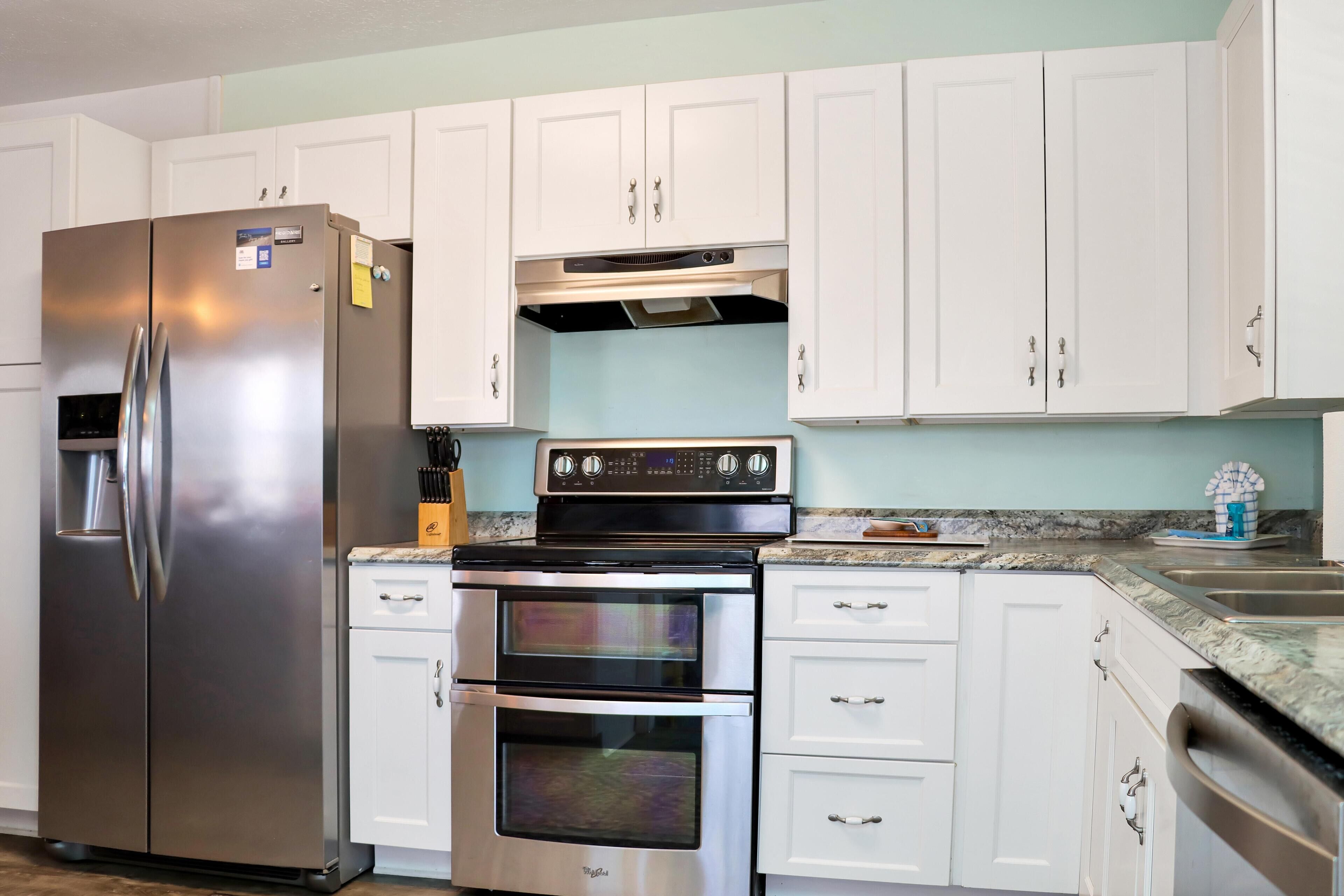 Una cocina con armarios blancos, un refrigerador de acero inoxidable, un horno doble y un microondas.