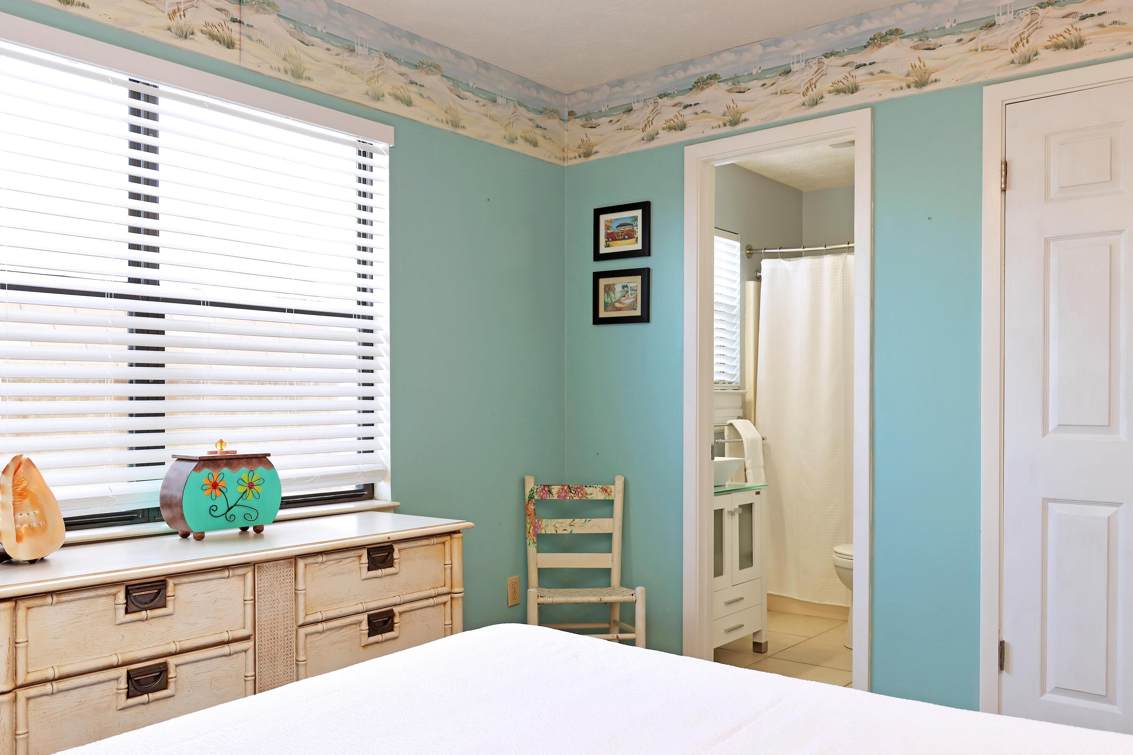 A bedroom with a bed, a dresser, a chair, and a window with blinds.