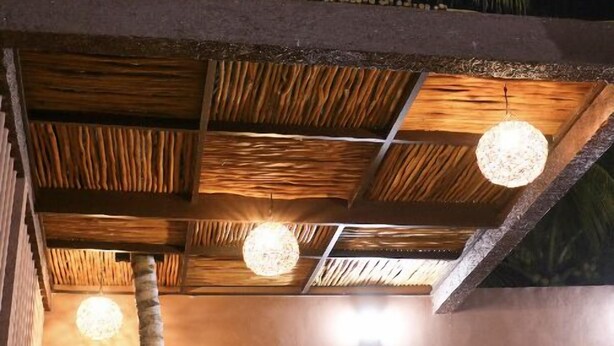 Ein Terrassenbereich im Freien mit Holzboden und hängenden, kugelförmigen Lampen. Zwei grüne Gestellstühle und ein kleiner Tisch sind ebenfalls vorhanden.