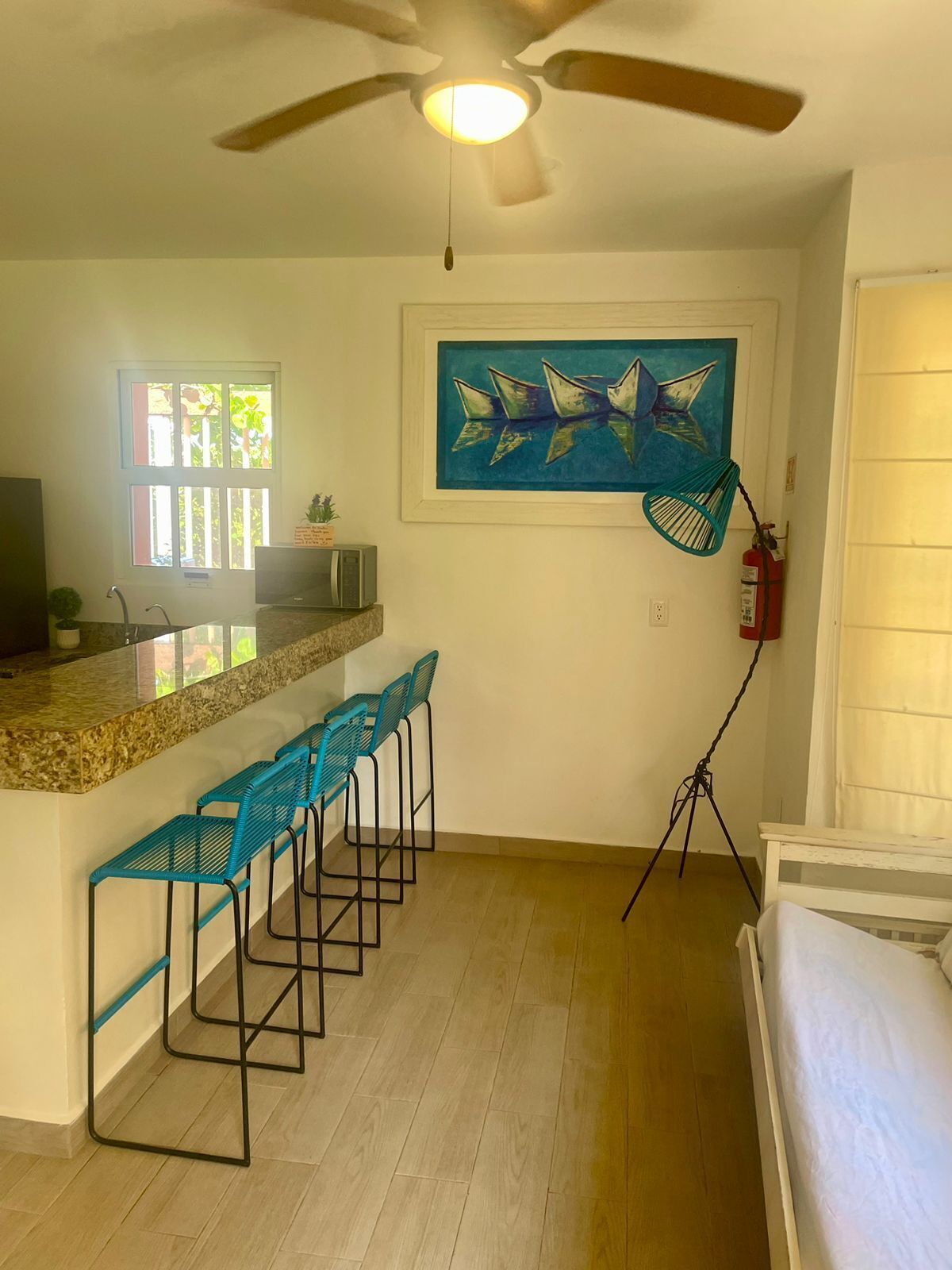 A kitchen with a bar area, a ceiling fan, a painting, and a fire extinguisher.