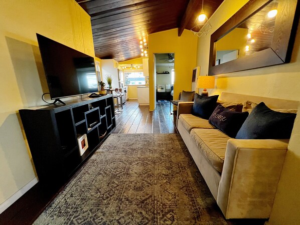 A living room with a sofa, a TV, and a coffee table. There is a hallway leading to another room.