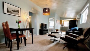 A spacious living room with a dining area, a large window, and a ceiling light fixture.