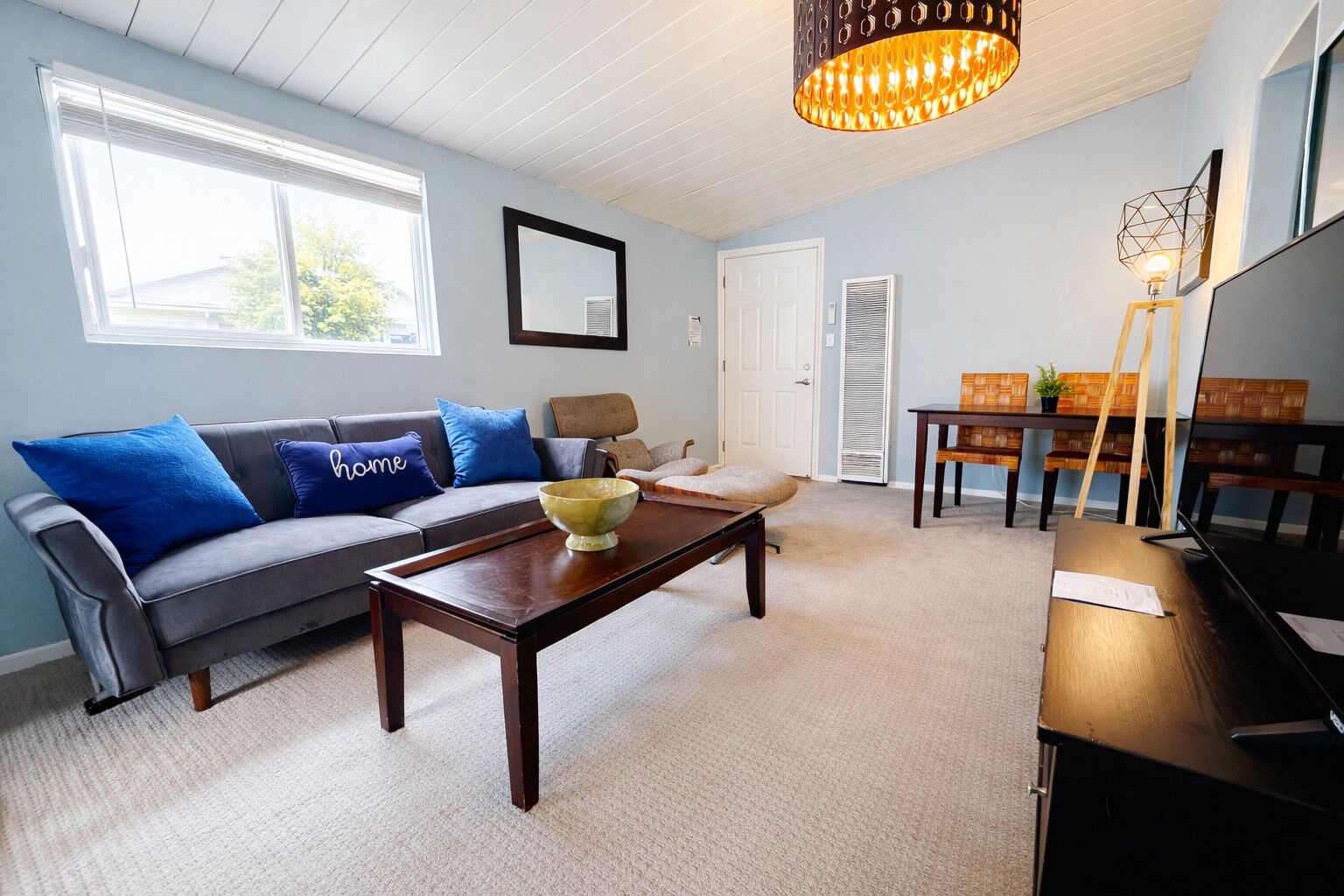 A living room with a sofa, coffee table, and a TV. There is a door and a window in the room.