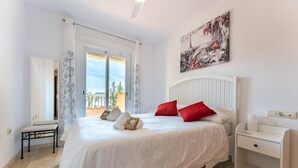 A bedroom with a large bed, a nightstand, a bench, and a view of the outdoors. - CT 232 - Eden Golf Sur - Southfacing Apartment (Mijas)
