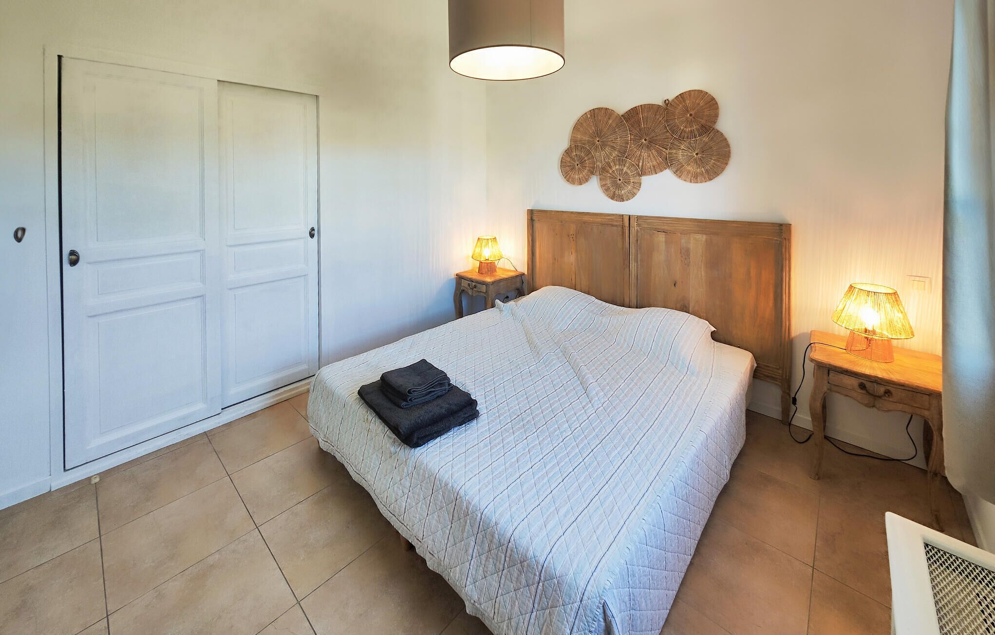 Een slaapkamer met een bed, twee bedlampen, een houten hoofdeinde, een kunstwerk aan de muur en een gesloten deur.