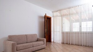 Ein Zimmer mit einem beigen Sofa, einer Holztür und einem Fenster mit durchsichtigen Vorhängen.