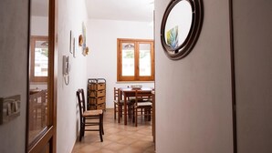 Ein Flur, der zu einem Essbereich mit Holzbänken und einem Tisch, einem Holzschrank und einem runden Spiegel an der Wand führt.