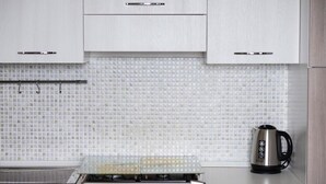 A kitchen with white cabinets, a tiled backsplash, and a kettle on the counter.