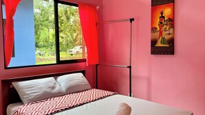 Een slaapkamer met een bed, een raam met rode gordijnen, een schilderij aan de muur en uitzicht op groen buiten.