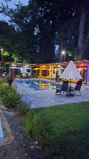 A pool area with lounge chairs and umbrellas, surrounded by a landscaped garden and a building with multiple windows. - Caribbean Blue Morpho (Puerto Viejo de Talamanca)