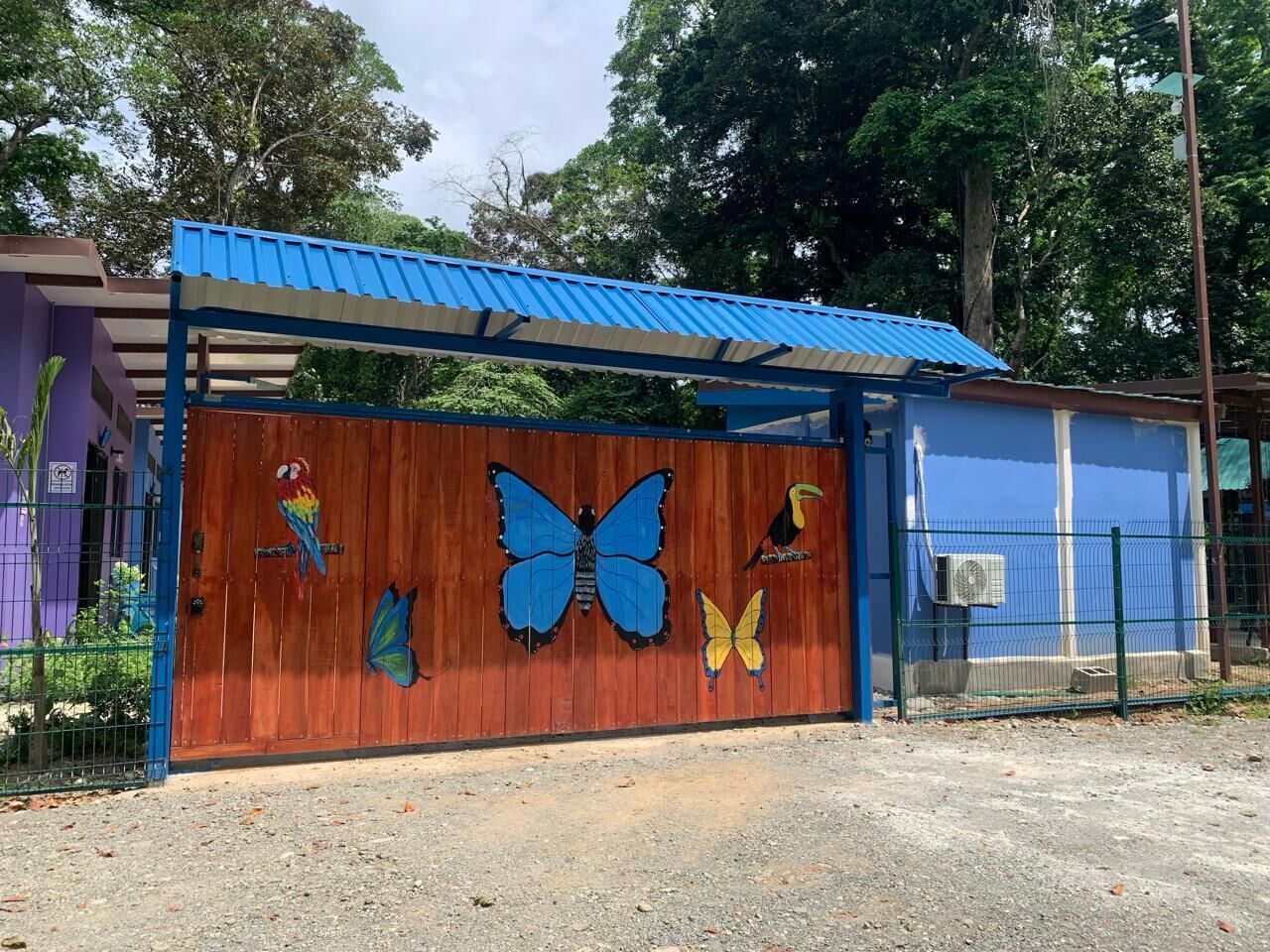 Um edifício com telhado azul e portão de madeira decorado com murais de borboletas e pássaros.