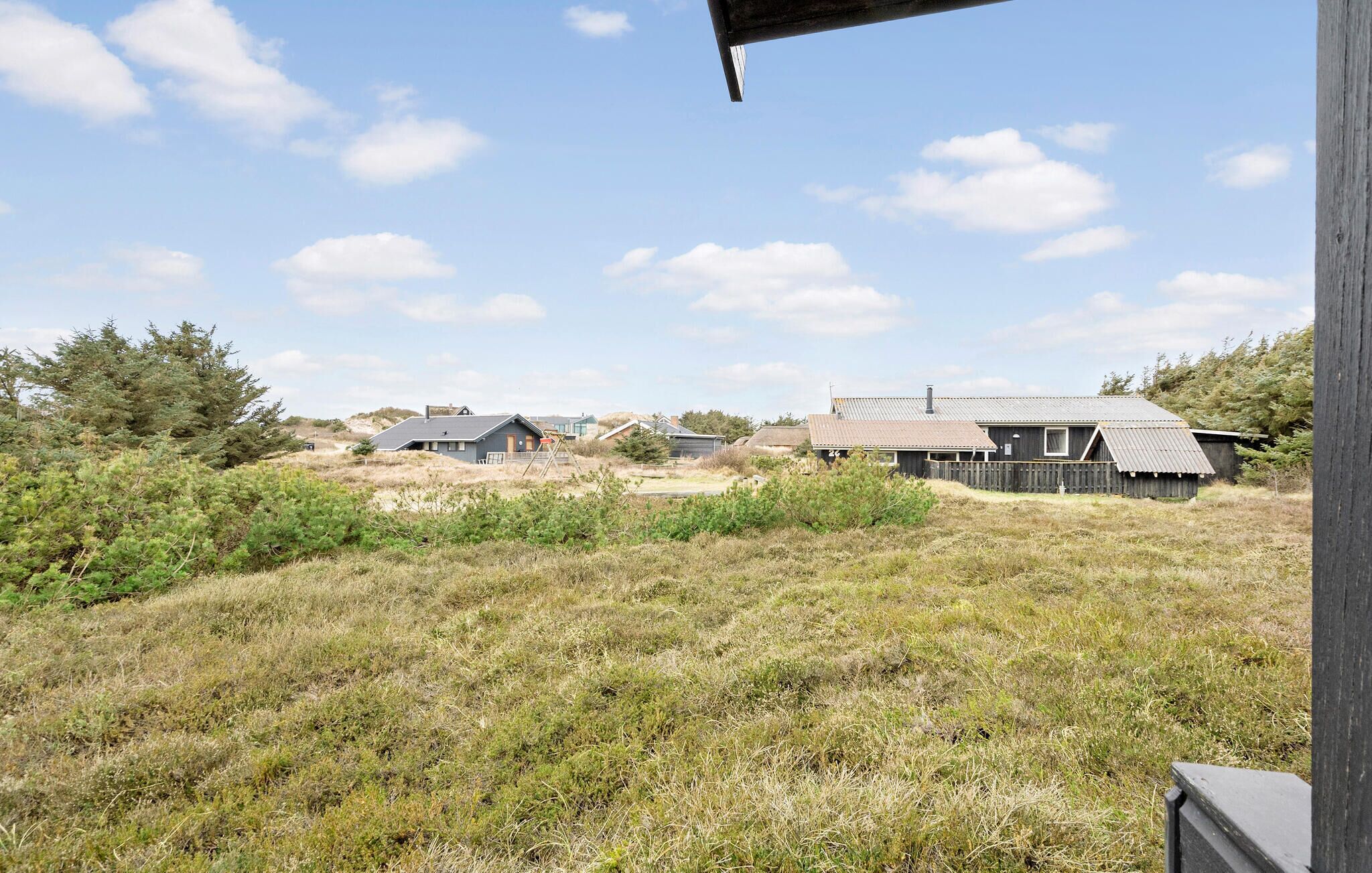 A rural landscape with several wooden buildings, including a house with a sloped roof and a barn-like structure.