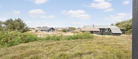 A rural landscape with several wooden buildings, including a house with a sloped roof and a barn-like structure.