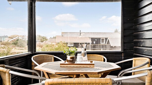 Un espace extérieur accueillant, aménagé avec des fauteuils en osier et une table ronde, offrant une vue sur un quartier résidentiel avec ses maisons et sa verdure.