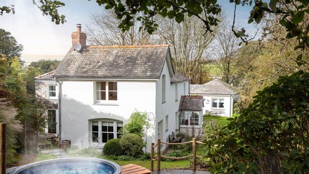 A white house with a brick chimney, a hot tub, and a smaller house in the background. - Calenick -  a stylish cottage that sleeps 6 guests  in 3 bedrooms (Trelights)