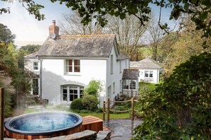 A white house with a brick chimney, a hot tub, and a smaller house in the background. - Calenick -  a stylish cottage that sleeps 6 guests  in 3 bedrooms (Trelights)