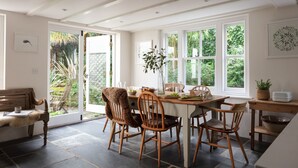 A dining area with a wooden table and chairs, a bench, and a view of greenery outside. - Calenick -  a stylish cottage that sleeps 6 guests  in 3 bedrooms (Trelights)