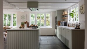 A modern kitchen with a central island, large windows, and a view of greenery outside. - Calenick -  a stylish cottage that sleeps 6 guests  in 3 bedrooms (Trelights)