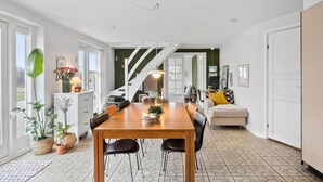 Ein geräumiger Essbereich mit Holztisch und Stühlen, eine Treppe, die in einen anderen Raum führt, und eine gemütliche Sitzecke mit Kissen.