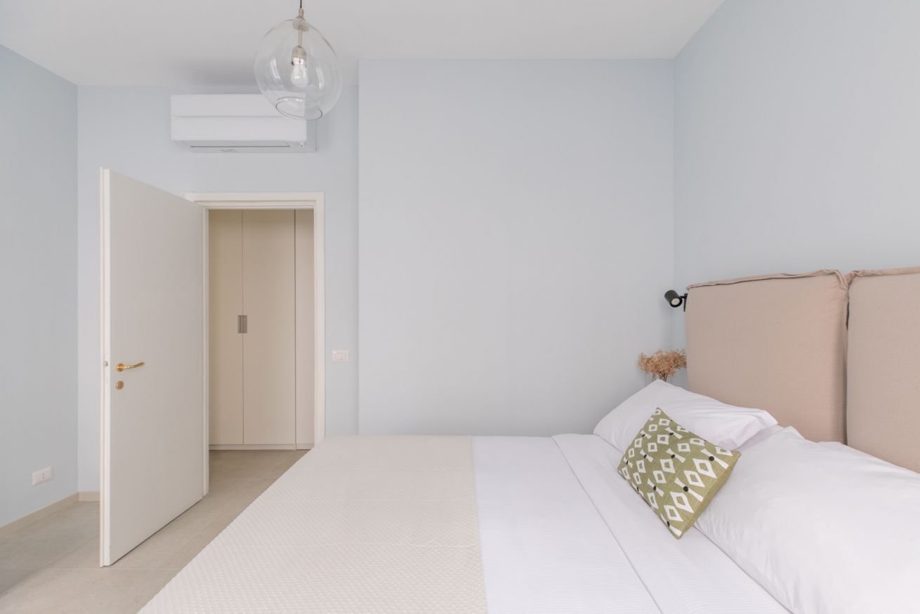 A bedroom with a bed, a door, a light fixture, and a wall-mounted air conditioner.