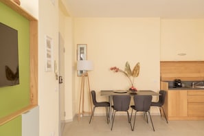 A compact kitchen with a dining area, a standing lamp, and a vase with flowers.