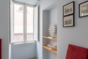 Una habitación con ventana, un sofá rojo y dos cuadros en la pared.
