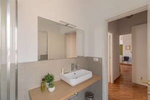 Une salle de bain moderne avec un grand miroir, un lavabo blanc et une petite plante posée sur le meuble-vasque.