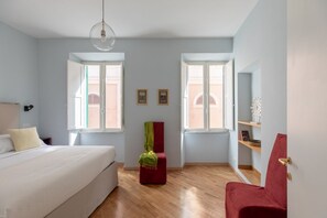 Une chambre à coucher avec un lit, deux fenêtres, une chaise rouge et un plancher en bois.