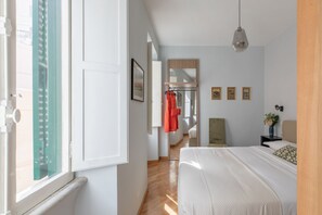 Et soveværelse med seng, et vindue med skodder, et spejl og et natbord med lampe.