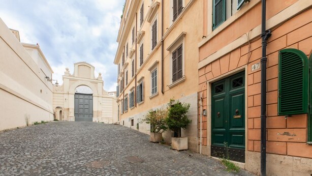 Una strada acciottolata con edifici storici, un cancello e una porta verde.