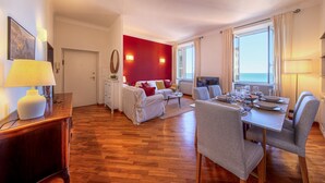 A modern hotel room with a wooden floor, a dining area with a table set for two, a bed with red walls, and a view of the sea through large windows. - 🏠 PROPERTY DESCRIPTIONCasa Valentina is located in a typical Ligurian building, in a central area near the charming harbor of Camogli.It is the perfect starting point for a seaside holiday without the need to use a car or public transport.In just 5 mi (Camogli)
