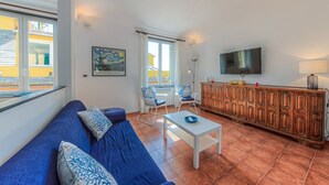 Ein Wohnzimmer mit einer Couch, Sesseln, einem Fernseher und einem Schrank.