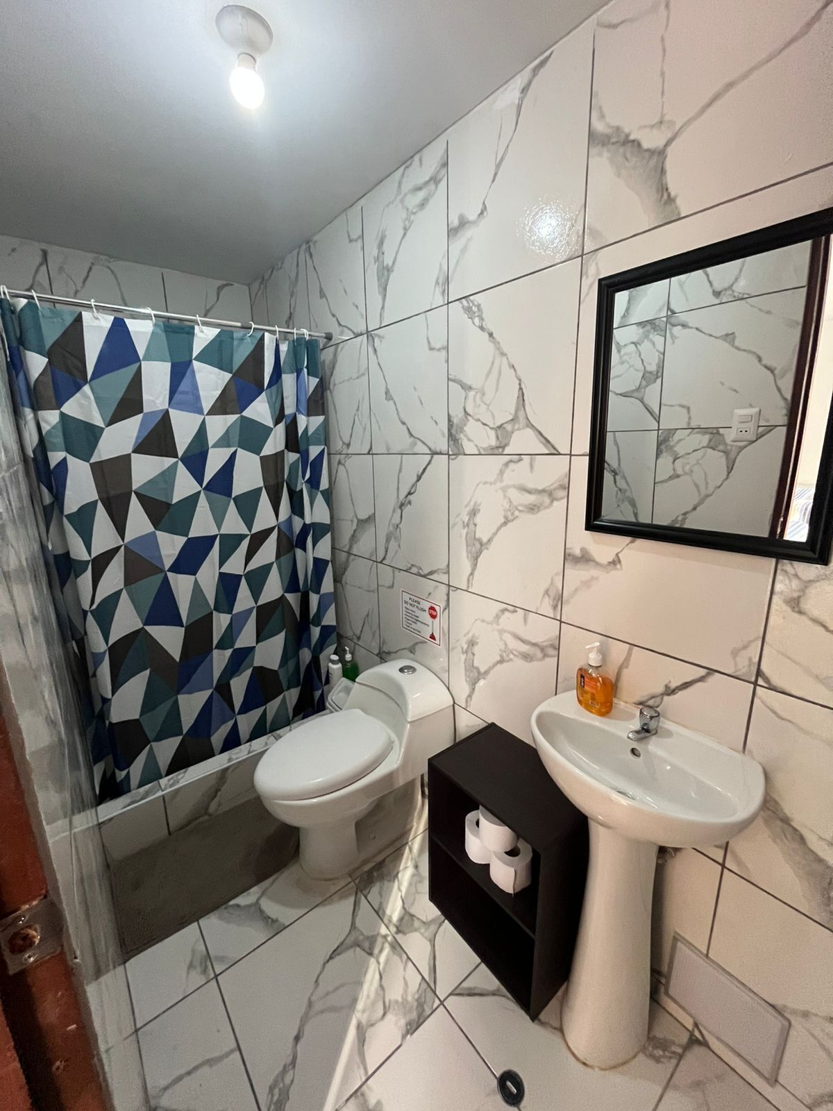 Une salle de bain avec un rideau de douche à motifs géométriques, deux toilettes, un lavabo et un miroir.