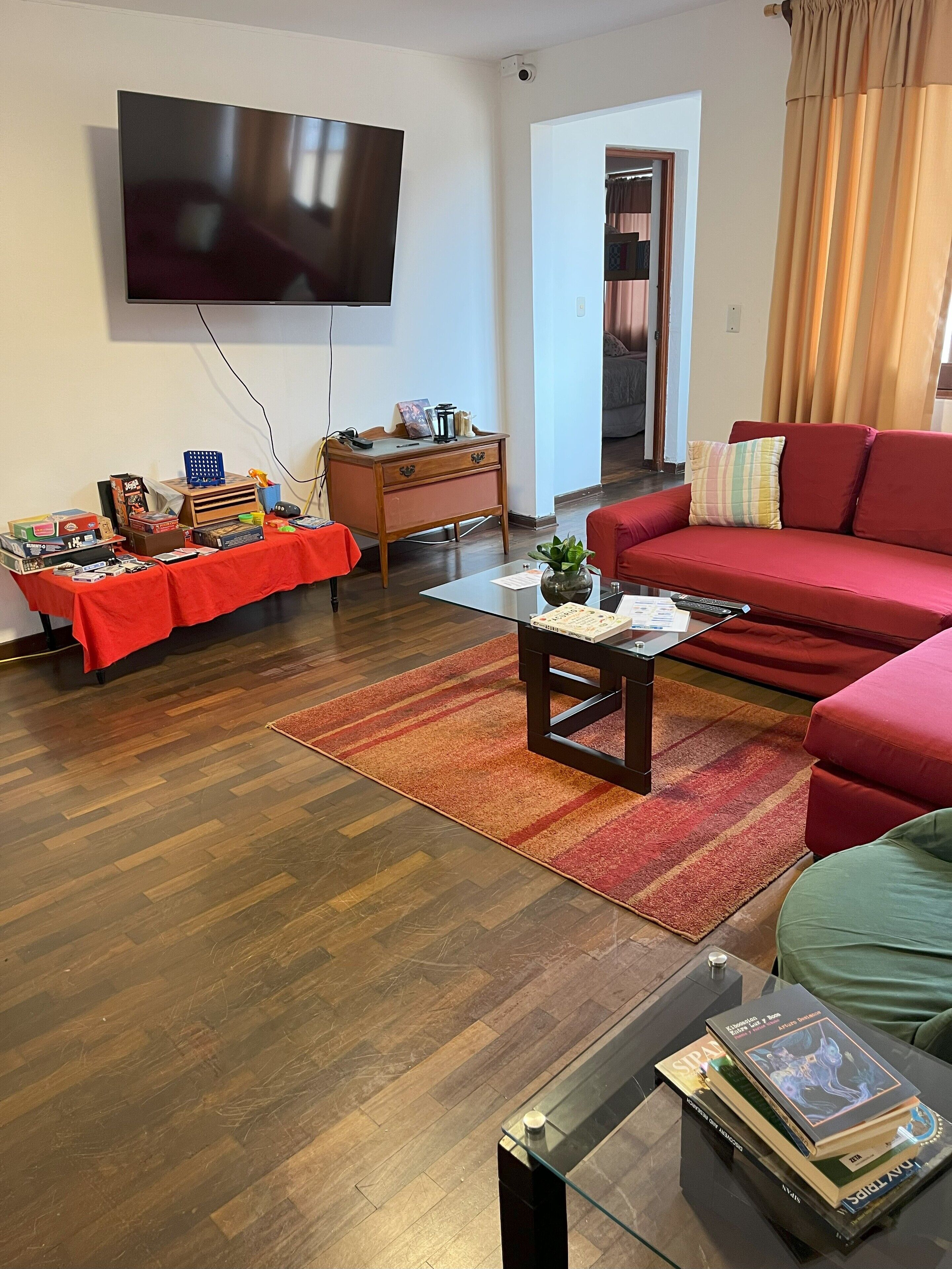 Una sala de estar con televisor de pantalla plana, un sofá rojo, una mesa de centro de vidrio y un mueble de madera.