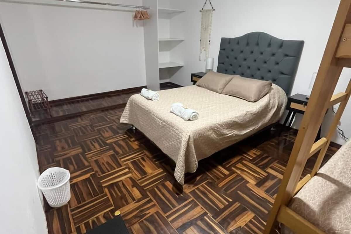 Un dormitorio con una cama, suelo de madera, una mesita y una silla.