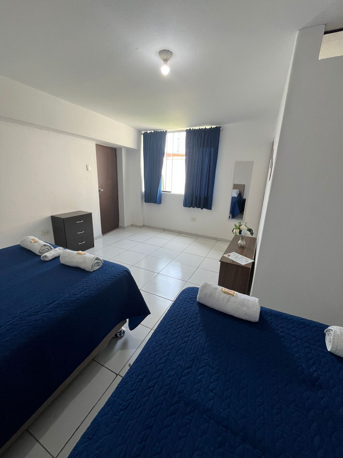 Habitación de hotel con dos camas, un escritorio pequeño, un espejo y una ventana con cortinas.