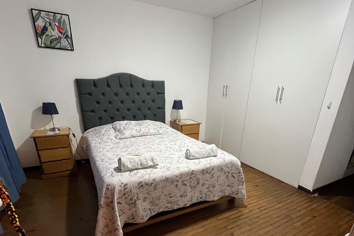 Un dormitorio con cama, dos mesitas de noche, un armario y un cuadro en la pared.