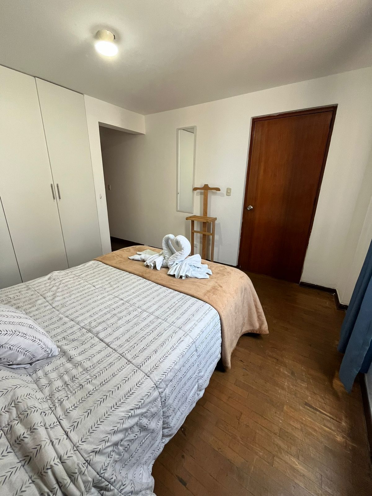 Une chambre à coucher avec un lit, une armoire en bois, un miroir et une porte.