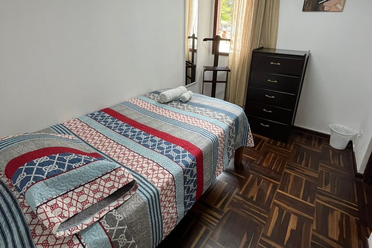 Un dormitorio con cama, cómoda, espejo y ventana con cortinas.