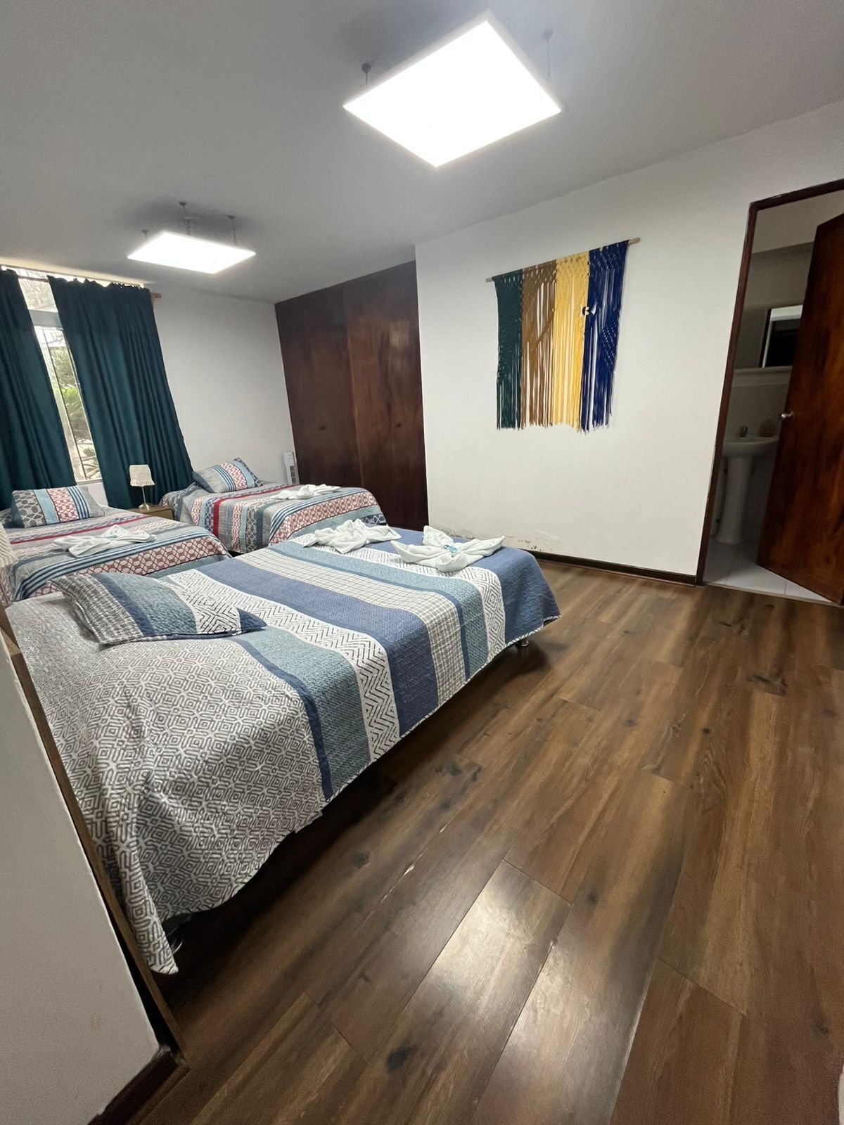Una habitación con dos camas, suelo de madera, un ventanal con cortinas y un tapiz colgando en la pared.