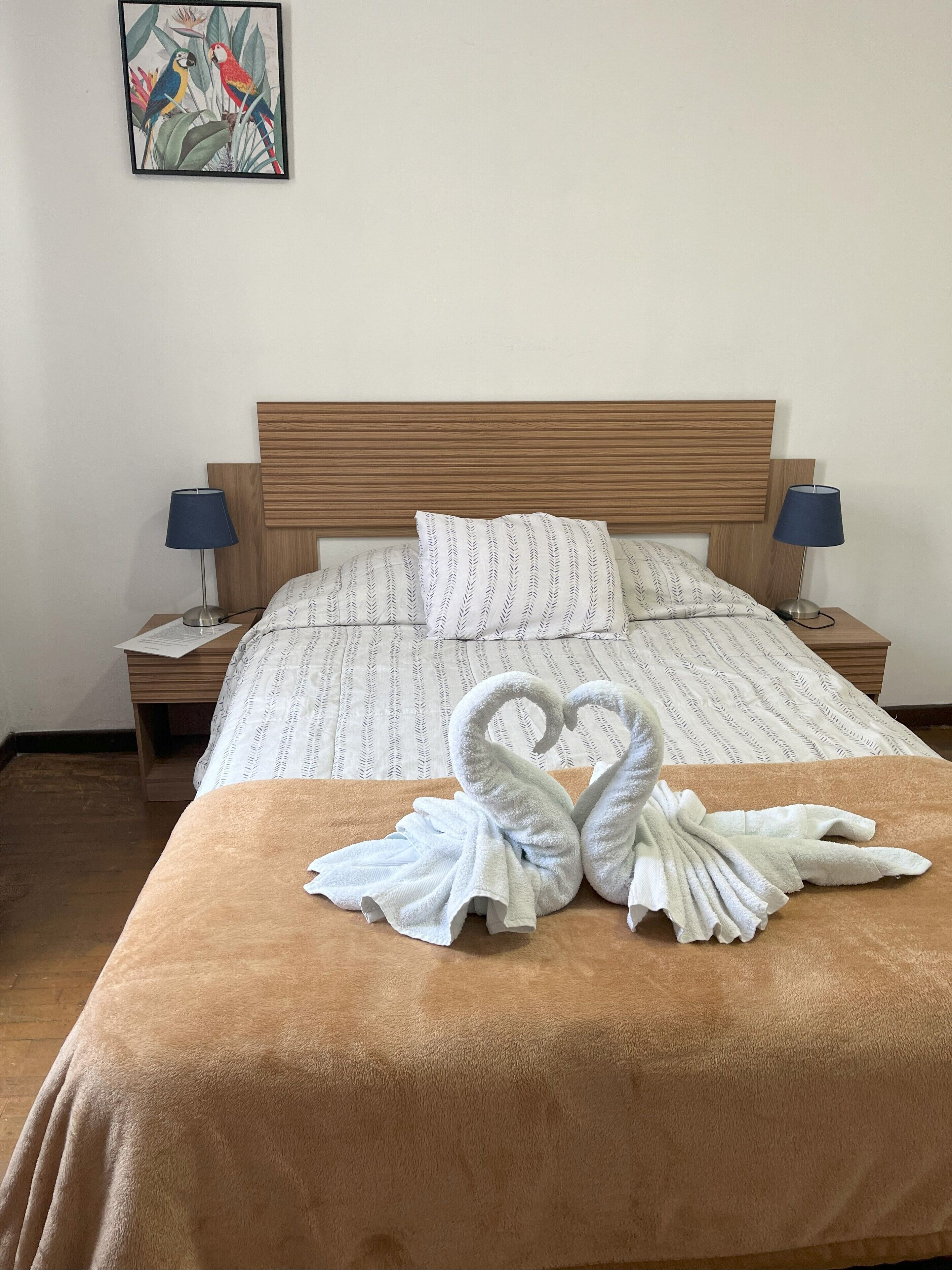 Cama bem arrumada com manta marrom, duas almofadas e arranjo de toalha em formato de coração na cama.