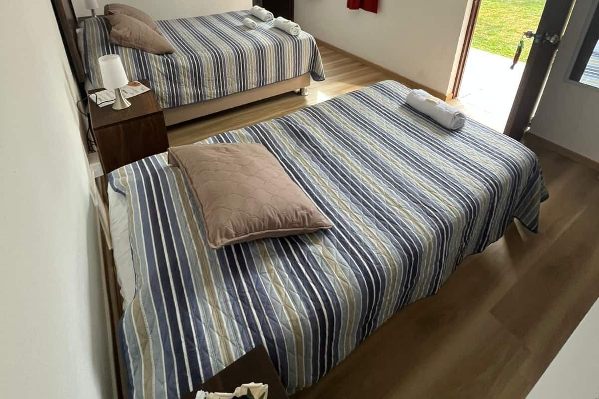 Una habitación con dos camas, una mesita de noche, una lámpara y un ventanal con cortinas rojas.