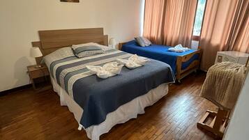 A bedroom with a large bed, a smaller bed, a wooden chair, a nightstand, a lamp, and a painting on the wall.