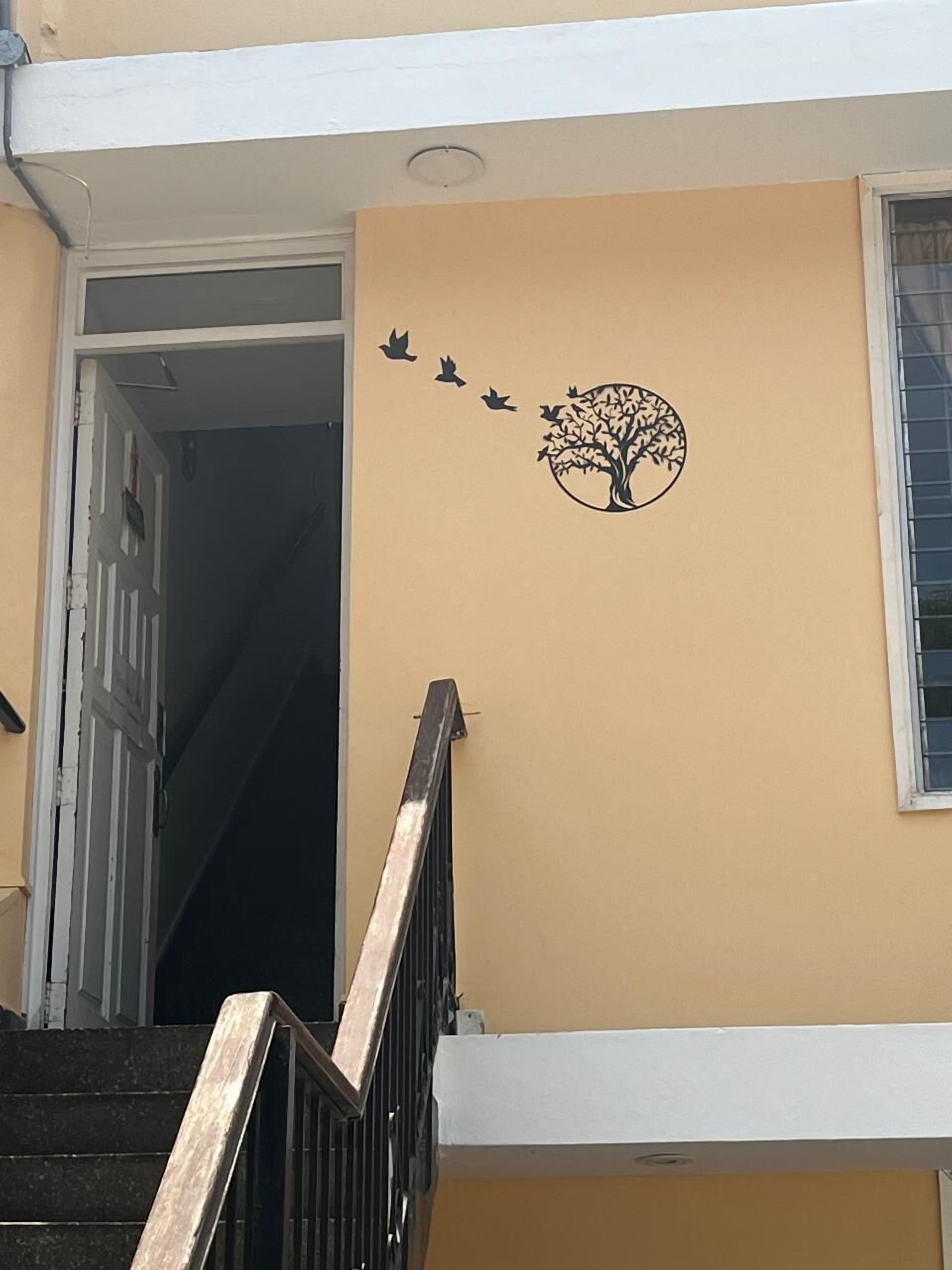 A beige wall with a tree and birds decal, a window, and a staircase with a metal handrail.